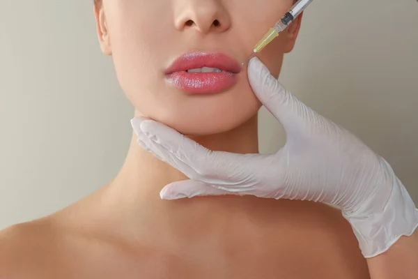 Woman getting lip injection on beige background, closeup