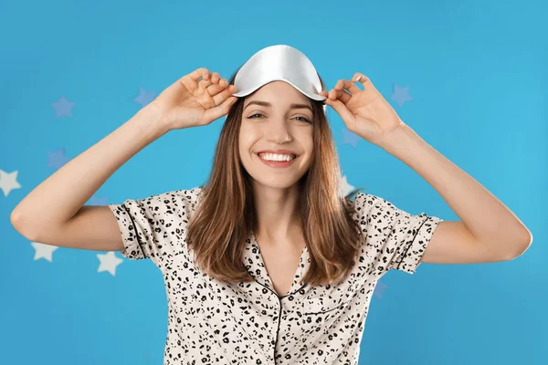 Beautiful woman wearing pajamas and sleep mask on light blue bac — Stock Photo, Image