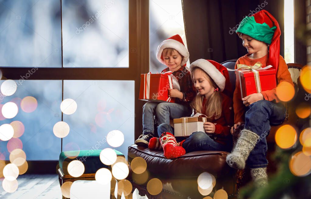 Little children with Christmas gifts near window indoors. Presen