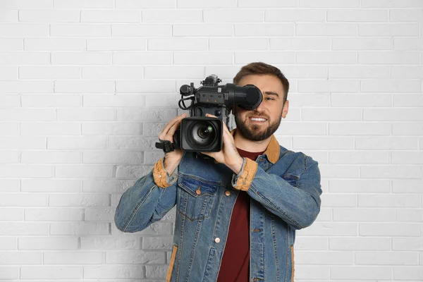 Operatör med professionell videokamera nära vit tegelvägg — Stockfoto