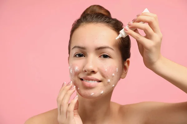 Teen girl with acne problem applying cream on light pink backgro — Stock Photo, Image