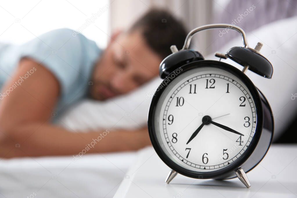 Man sleeping at home in morning, focus on alarm clock. Space for
