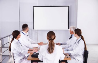 Doktorlar konferans sırasında kapalı alanda video projektörü kullanıyorlar.