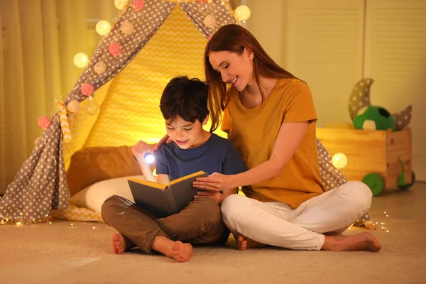 Matka a syn s baterkou čtení knihy doma — Stock fotografie