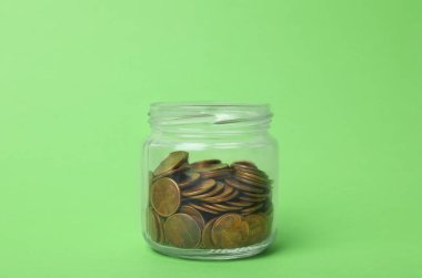 Açık yeşil zemin üzerinde bozuk paralar olan cam kavanoz