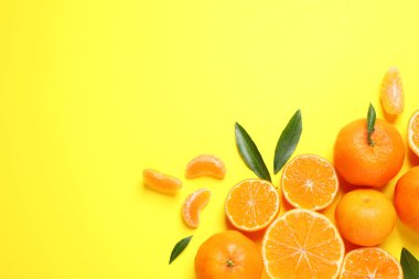 Düz kompozisyon, taze olgun mandalinalar ve sarı arka planda yapraklar, yazı için boşluk. Citrus meyvesi.