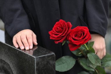 Siyah granit mezar taşının yanında kırmızı gülleri olan bir kadın.