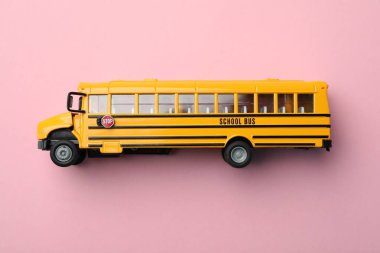Pembe arka planda sarı okul otobüsü, üst manzara. Öğrenciler için taşıma