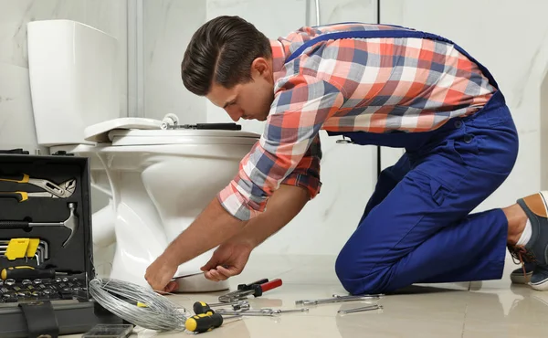 Профессиональный сантехник работает с унитазом в ванной комнате — стоковое фото