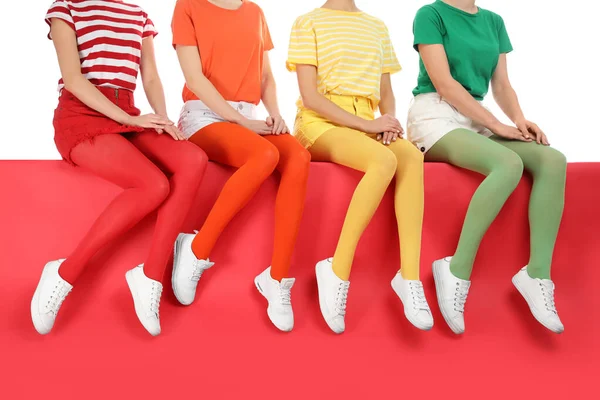 Mujeres con medias brillantes sentadas juntas sobre fondo de color — Foto de Stock