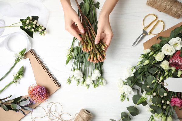 Florist making beautiful bouquet at white wooden table, top view