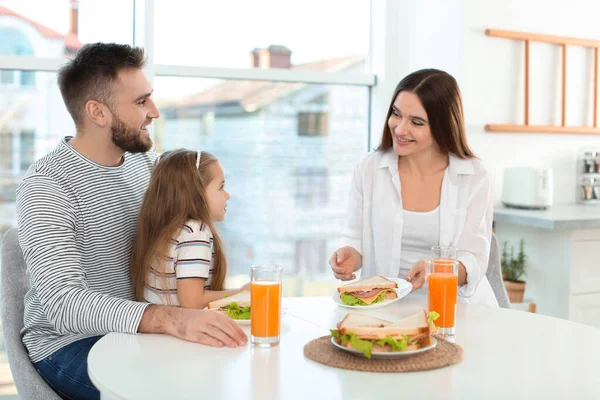 Família feliz tomando café da manhã com sanduíches à mesa na cozinha — Fotografia de Stock