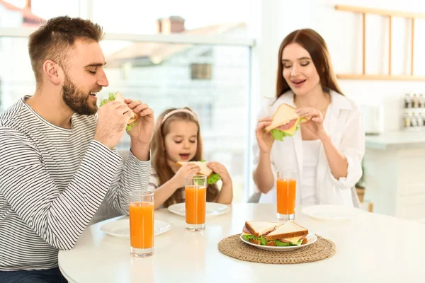 Šťastná rodina snídá se sendviči u stolu v kuchyni — Stock fotografie