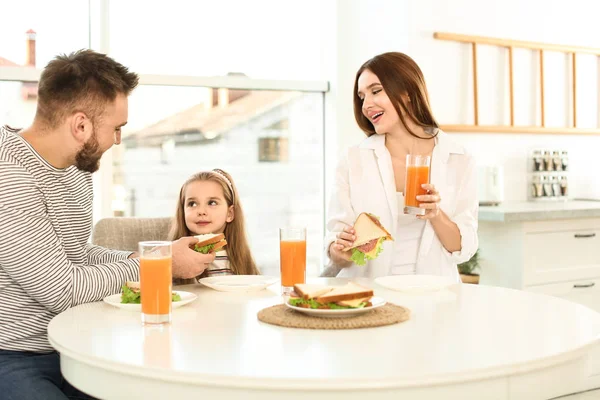 Šťastná rodina snídá se sendviči u stolu v kuchyni — Stock fotografie