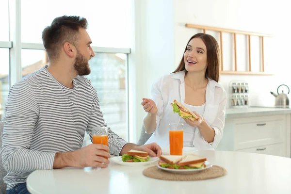 Szczęśliwa para je śniadanie z kanapkami przy stole w kuchni — Zdjęcie stockowe