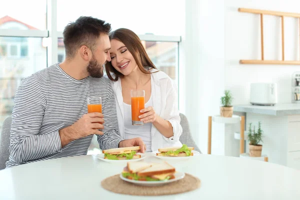 Happy couple having breakfast with sandwiches at table in kitche — 스톡 사진