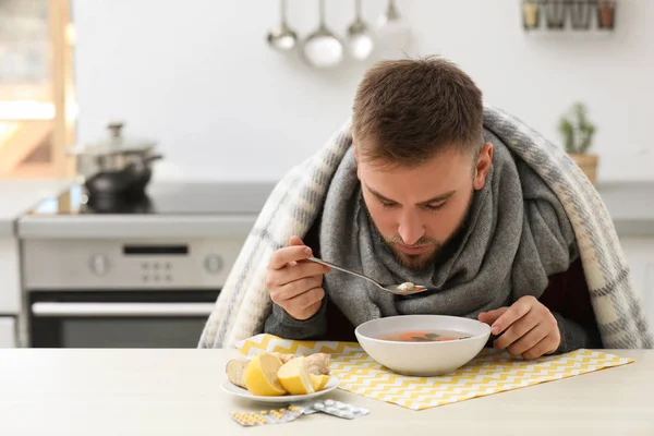 Jeune homme malade mangeant une soupe savoureuse pour guérir la grippe à table dans la cuisine — Photo