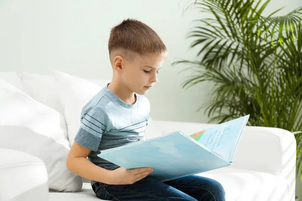 Kleiner Junge liest Buch auf Sofa drinnen — Stockfoto