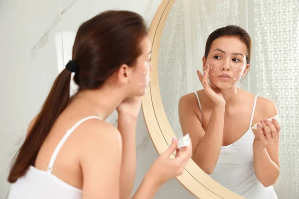 Chica adolescente con problemas de acné aplicando crema cerca del espejo en bathro — Foto de Stock