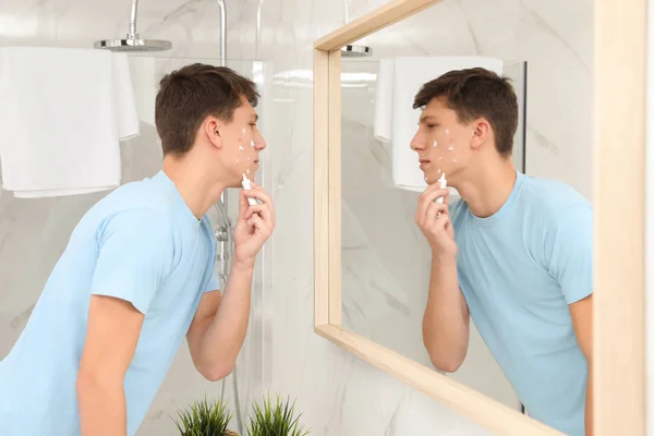 Teen guy with acne problem applying cream near mirror in bathroo — ストック写真