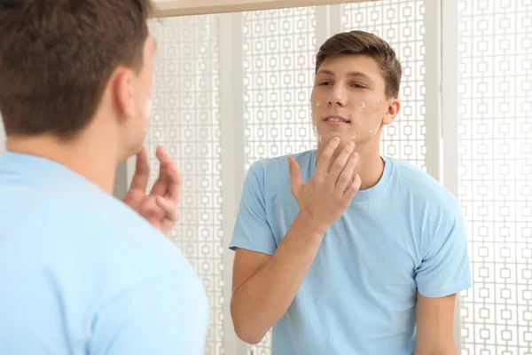 Adolescente cara com problema de acne aplicando creme perto do espelho dentro de casa — Fotografia de Stock
