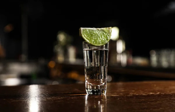 Mexican Tequila shot with lime slice on wooden bar counter