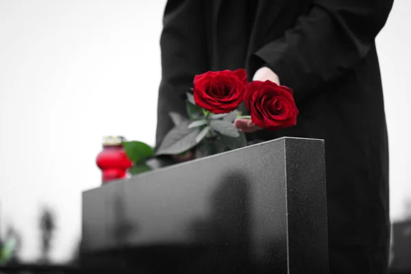 Женщина с красными розами возле черного гранитного надгробия на открытом воздухе, затылок — стоковое фото