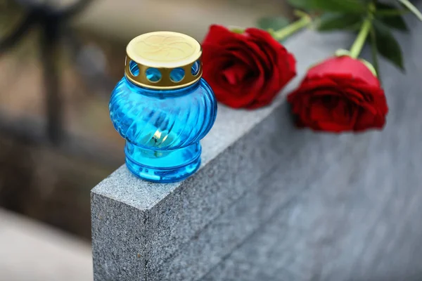 Red roses and candle on light grey tombstone outdoors, closeup.