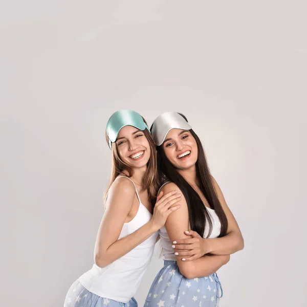 Hermosas mujeres con máscaras para dormir sobre fondo gris claro . — Foto de Stock