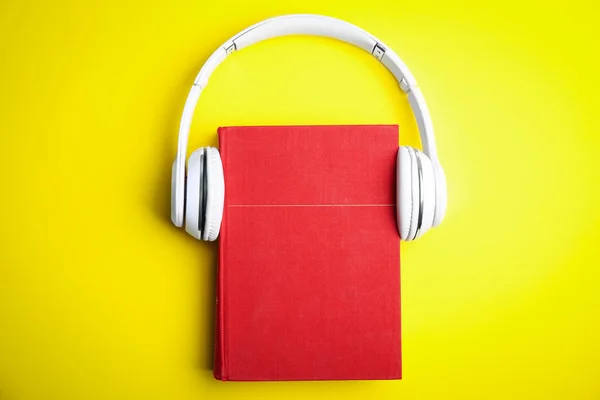 Książka i nowoczesne słuchawki na żółtym tle, widok z góry — Zdjęcie stockowe