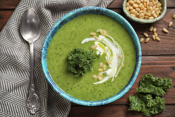 Tasty kale soup served on wooden table, flat lay