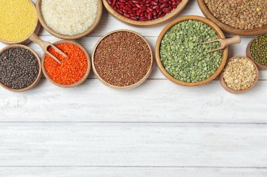 Düz kompozisyon, beyaz ahşap masa üzerinde farklı türde baklagiller ve tahıl gevrekleri, yazı için boşluk. Organik taneler