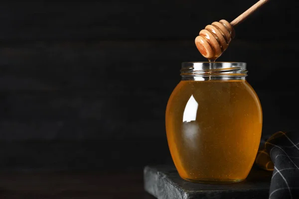 Tarro de miel orgánica y cazo en mesa de madera contra bac oscuro — Foto de Stock