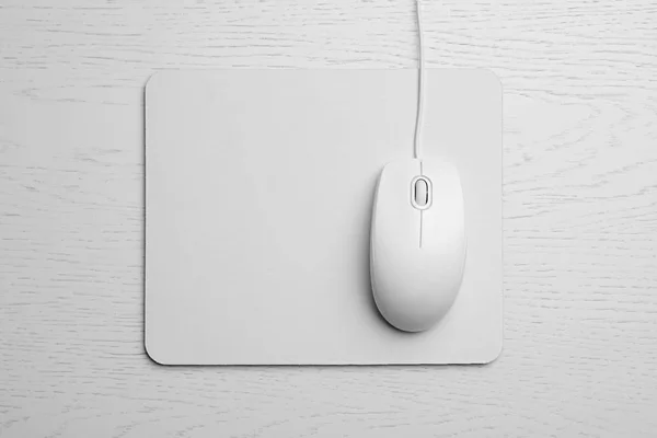 Wired computer mouse and pad on white wooden background, flat lay. Space for text