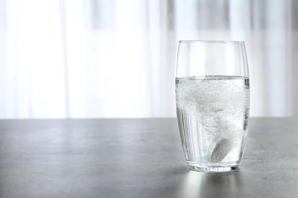 Glass with effervescent tablet on grey table indoors, space for text. Medical care