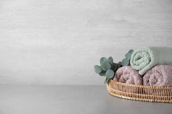 Wicker tray with rolled bath towels and eucalyptus branch on gre — Stock Photo, Image