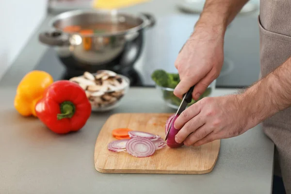 Jonge man snijden groenten voor soep in de keuken, close-up — Stockfoto