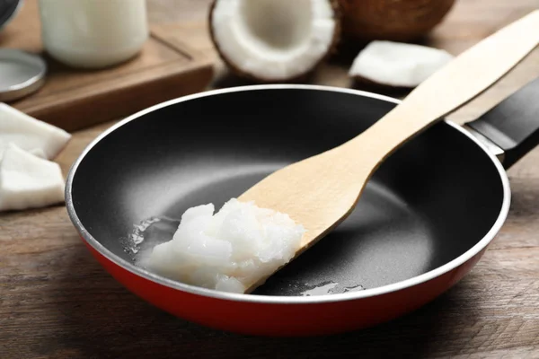 Frying pan with coconut oil and wooden spatula on wooden table. — Stock Photo, Image