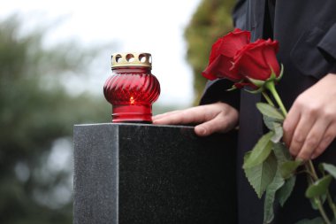 Woman holding red roses near black granite tombstone with candle clipart