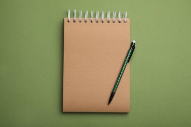 Yeşil arkaplanda Kraft defter ve kalem, üst görünüm