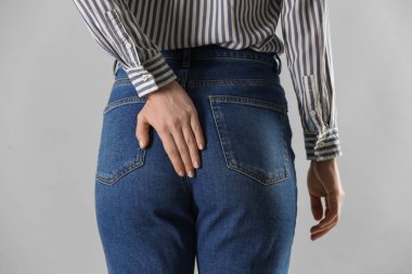 Açık gri arka planda hemoroitten muzdarip kadın, yakın plan.