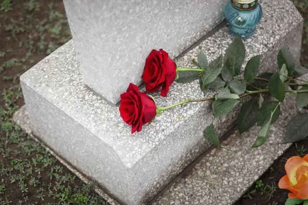 Red roses and candle on old grey tombstone outdoors. Funeral cer