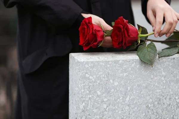 Жінка з червоними трояндами біля світло-сірого надгробного каменю на відкритому повітрі, крупним планом — стокове фото