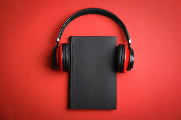 Boek en moderne koptelefoon op rode achtergrond, bovenaanzicht — Stockfoto
