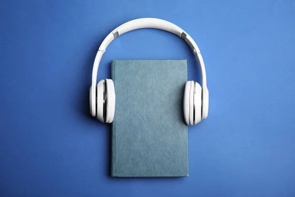 Libro y auriculares modernos sobre fondo azul, vista superior — Foto de Stock