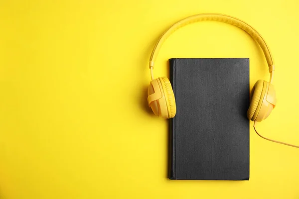 Βιβλίο και σύγχρονα ακουστικά σε κίτρινο φόντο, πάνω άποψη. Διάστημα — Φωτογραφία Αρχείου