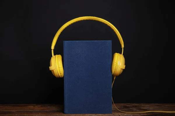 Boek en moderne koptelefoon op houten tafel tegen zwarte backgro — Stockfoto