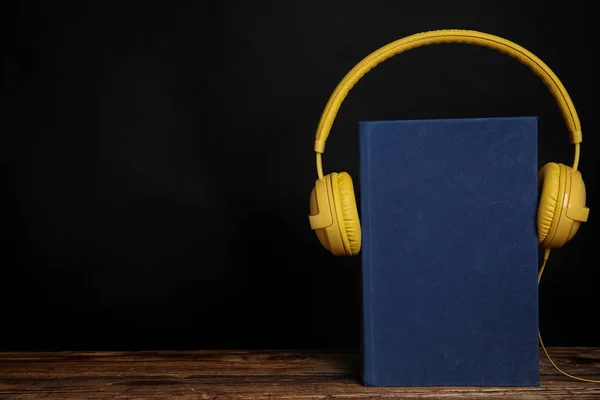 Boek en moderne koptelefoon op houten tafel tegen zwarte backgro — Stockfoto