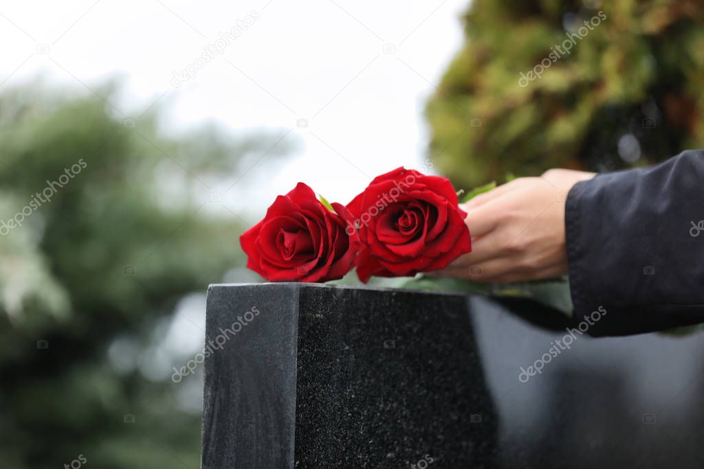 Woman with red roses near black granite tombstone outdoors, clos