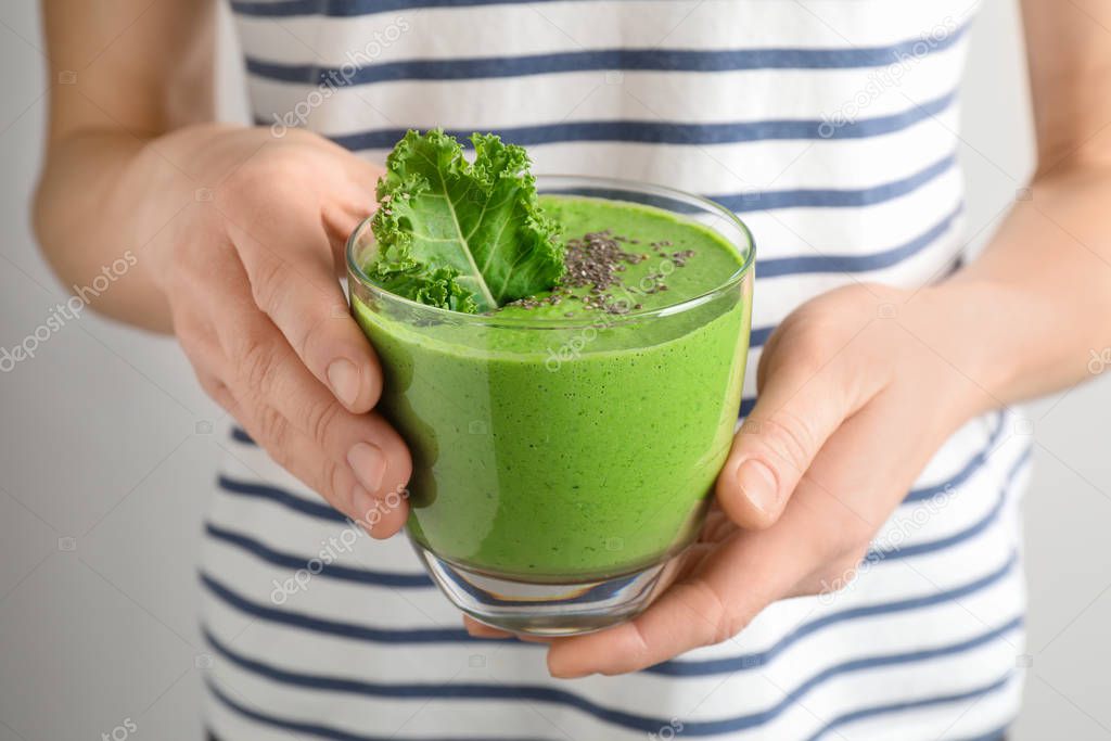 Woman holding tasty kale smoothie with chia seeds on light background, closeup